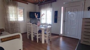 A room with a dining table, chairs, a TV, and a door. - garden house nafplio (Nafplio)