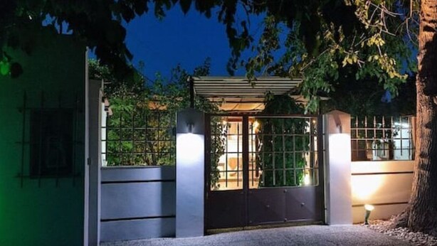 A gated entrance with a metal gate and a small covered area with a roof, surrounded by trees and a building in the background. - garden house nafplio (Nafplio)