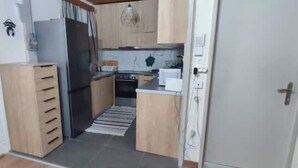 A compact kitchen with wooden cabinets, a refrigerator, and a stove. - garden house nafplio (Nafplio)