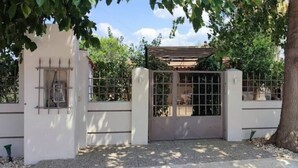 A gated entrance with a metal gate and a small window, surrounded by trees and a white wall. - garden house nafplio (Nafplio)