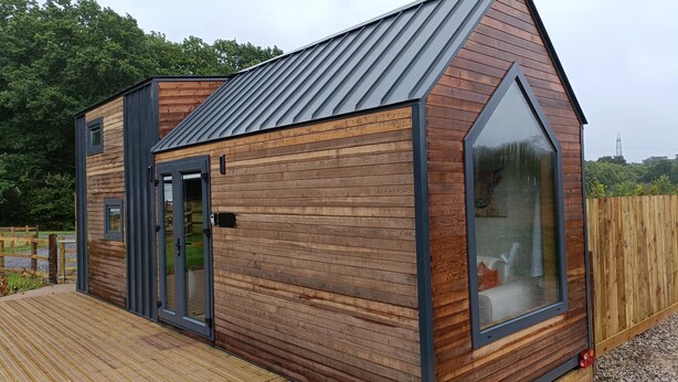 A modern wooden cabin with a sloped roof, large windows, and a deck. - The Tiny House  -  a dunley cottages - devon that sleeps 2 guests  in 1 bedroom (Bovey Tracey)