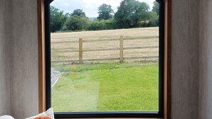 A room with a large window, a wooden ceiling, and a view of a grassy field. - The Tiny House  -  a dunley cottages - devon that sleeps 2 guests  in 1 bedroom (Bovey Tracey)