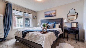 Une chambre à coucher comprenant un lit, un bureau, une chaise, une fenêtre avec des rideaux, un tableau au mur et un miroir.