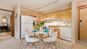Une cuisine moderne avec des meubles en bois, un réfrigérateur blanc et un coin repas comprenant une table ronde et des chaises blanches.