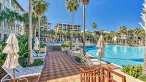 Zona de piscina hotelera con tumbonas, palmeras y suelo a cuadros.