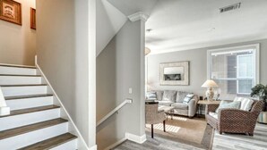 Una escalera conduce a un salón con suelo gris, un sofá y una mesa de centro.