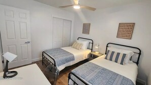 Une chambre avec deux lits, un ventilateur de plafond, une table de chevet avec une lampe et un Galaxy S22 Ultra posé sur une table.