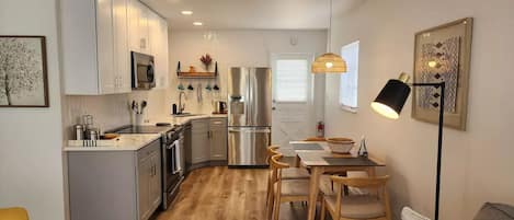 A modern kitchen with white cabinets, stainless steel appliances, and a dining area with wooden chairs and a table.
