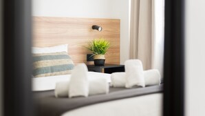 A modern hotel room with a wooden headboard, a bedside plant, a striped pillow, and white chairs. - Pascal Home By CanariasGetaway (Las Palmas de Gran Canaria)