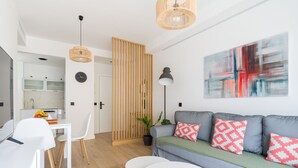 A modern living room with a grey sofa, white chairs, a dining table, and a kitchen in the background. - Pascal Home By CanariasGetaway (Las Palmas de Gran Canaria)