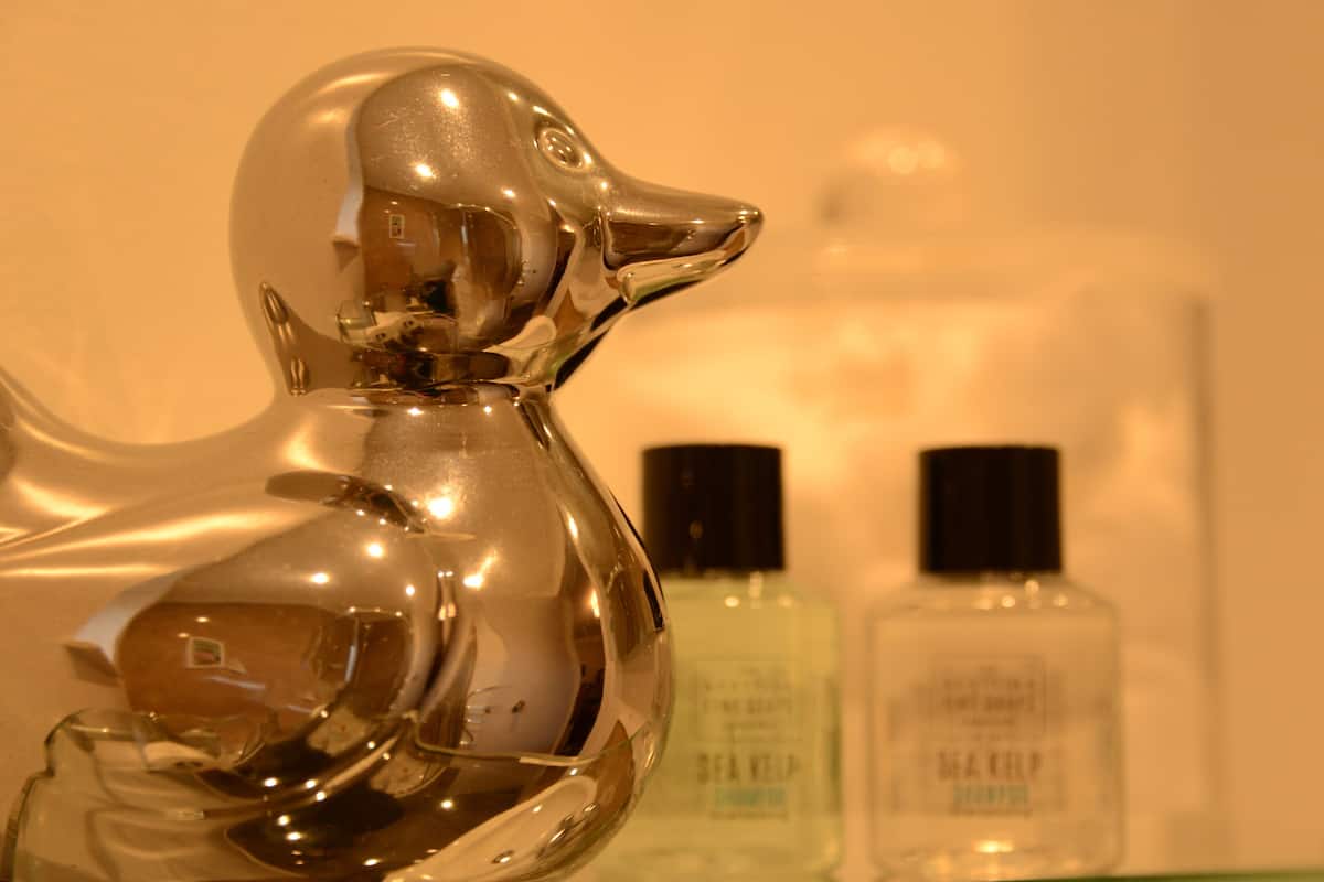A bathroom with a chrome dog-shaped soap dispenser and two bottles of shampoo.