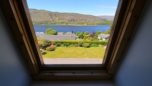 A skylight window with a view of a lake, surrounding greenery, and distant hills. - Lochview Guest House (Fort William)