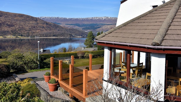 A lakeside property with a wooden deck, a dining area with outdoor seating, and a view of a lake and mountains. - Lochview Guest House (Fort William)