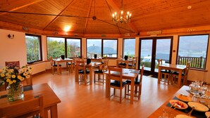 A wooden interior with tables and chairs, large windows with a view of the outdoors, and a chandelier. - Lochview Guest House (Fort William)