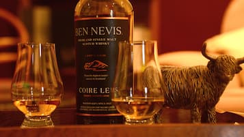 A bottle of Ben Nevis Highland Single Malt Scotch Whisky, two glasses, and a bull figurine on a wooden surface.