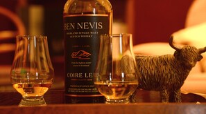 Une bouteille de Ben Nevis Highland Single Malt Scotch Whisky, deux verres et une figurine de taureau sur une surface en bois.