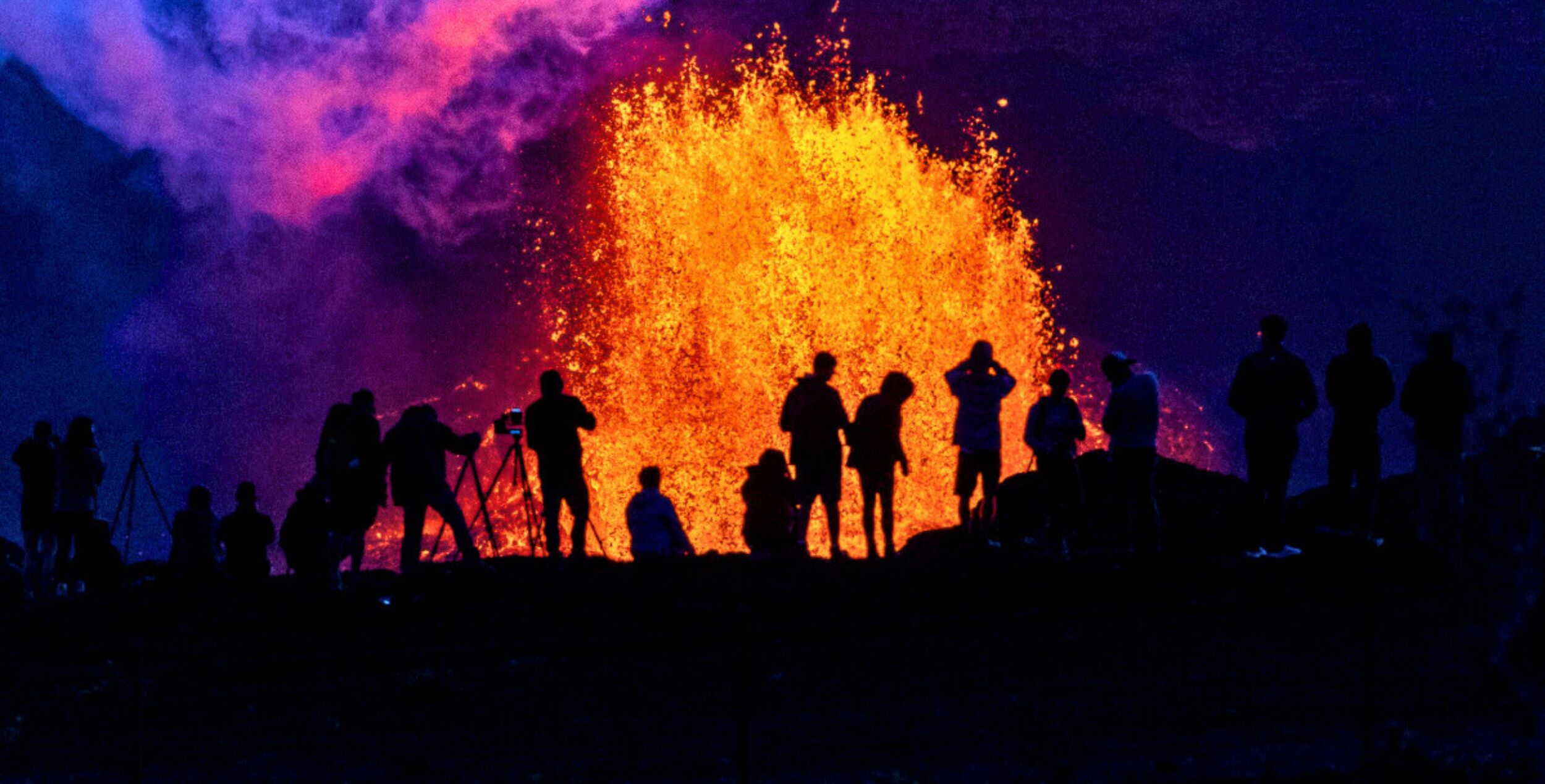 Silhouetten von Menschen, die einen Vulkanausbruch mit Rauch und Lava im Hawaii Volcanoes Nationalpark beobachten.
