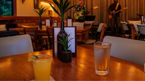 Un restaurante con una mesa de madera, un atril para el menú, un vaso de agua y una planta en un jarrón.
