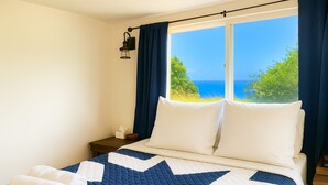 Un dormitorio con una cama grande, una mesita de noche, una ventana con cortinas y vistas al mar.
