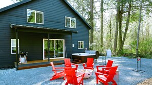 Ein modernes Haus mit überdachter Terrasse, roten Adirondack-Stühlen, einer Feuerstelle und einem Whirlpool.