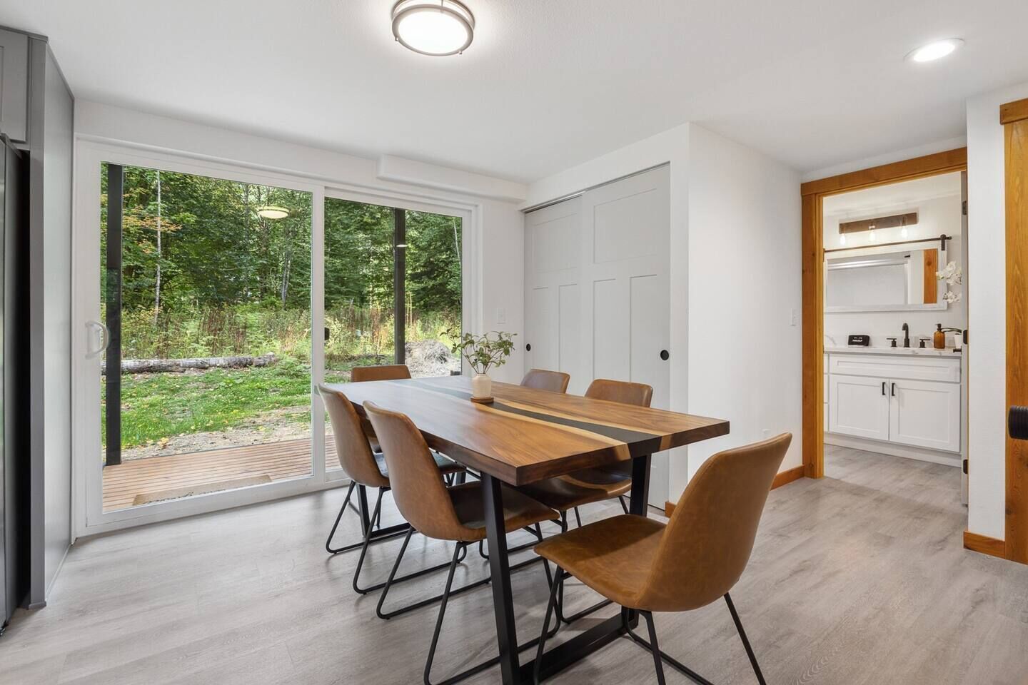 En moderne spisesalon med et stort træbord og seks stole, en skydedør til en have, samt et køkken med hvide skabe og en træbordplade.