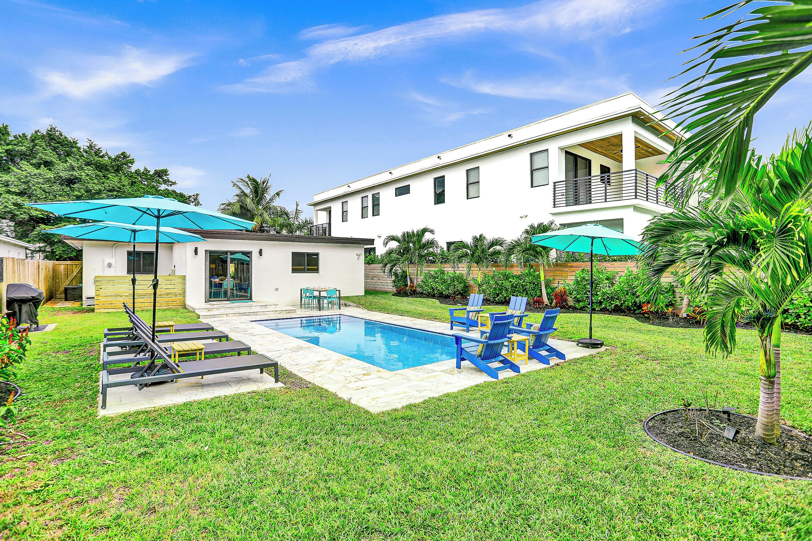 A backyard with a swimming pool, blue chairs, and umbrellas.