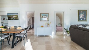 A spacious living area with a dining table set for four, a white cabinet, and a sofa. - 3419 Trullo Mest Marcucc by Perle di Puglia (San Michele Salentino)