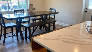 A modern kitchen with a marble countertop, a dining area with a wooden table and chairs, and a large window providing a view of the street. - Hidden Gem Modern Loft (Mission)