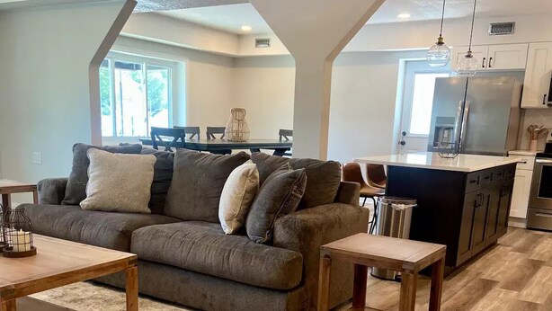 A modern living room with a sectional sofa, wooden coffee table, and a kitchen area with a refrigerator and island. - Hidden Gem Modern Loft (Mission)