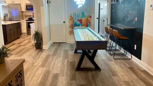 A modern kitchen with a built-in refrigerator, stove, and microwave. There is a dining area with a long table and bar stools. The walls are decorated with a neon sign and a chalkboard with "Welcome to the Mueller Building!" written on it. - Hidden Gem Modern Loft (Mission)