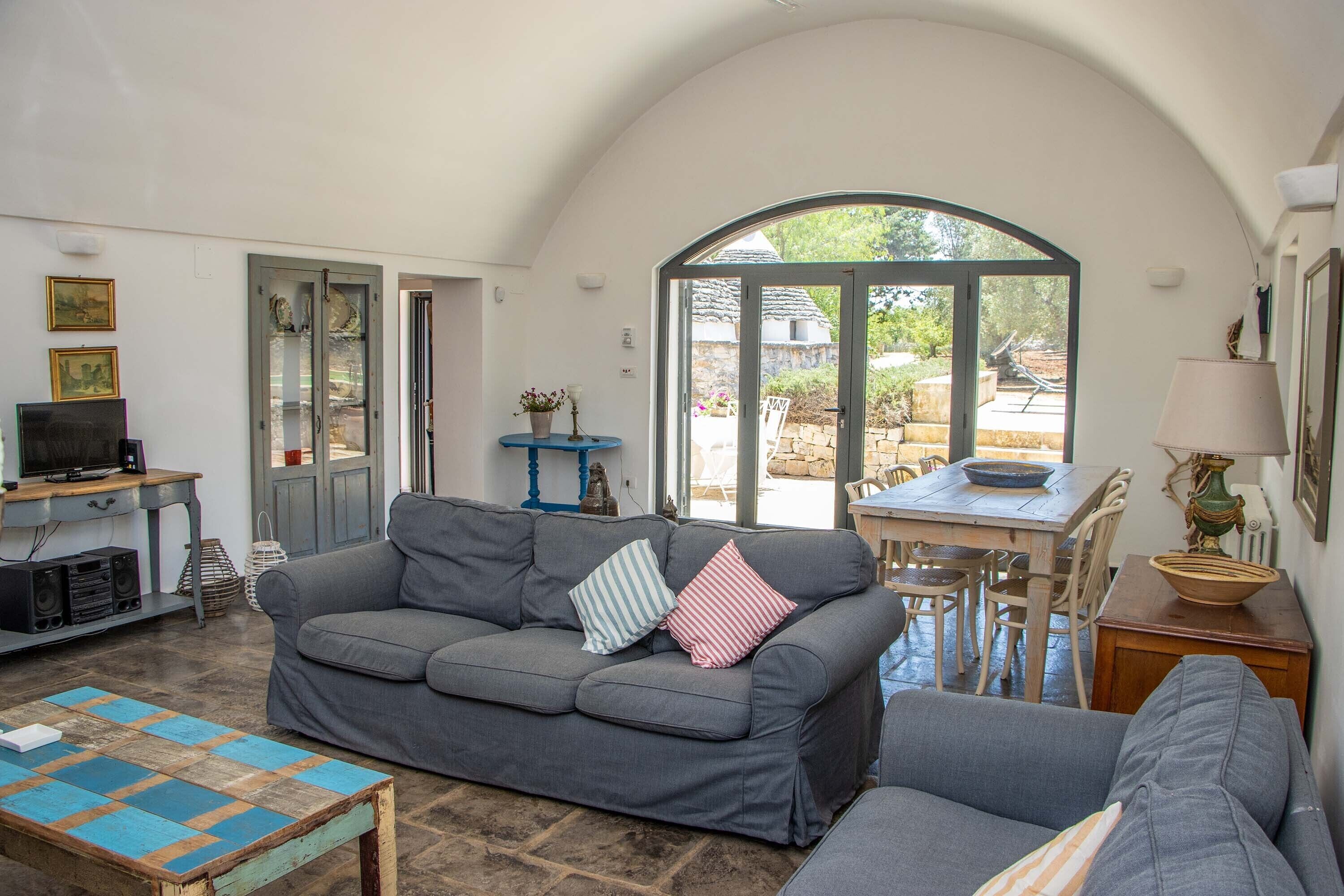 Ein gemütliches Wohnzimmer mit einer grauen Couch, einem Holztisch und einem Essbereich mit Tisch und Stühlen.