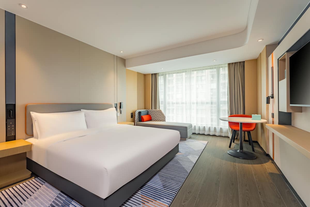 Una habitación de hotel moderna con una cama grande, un escritorio y un televisor.