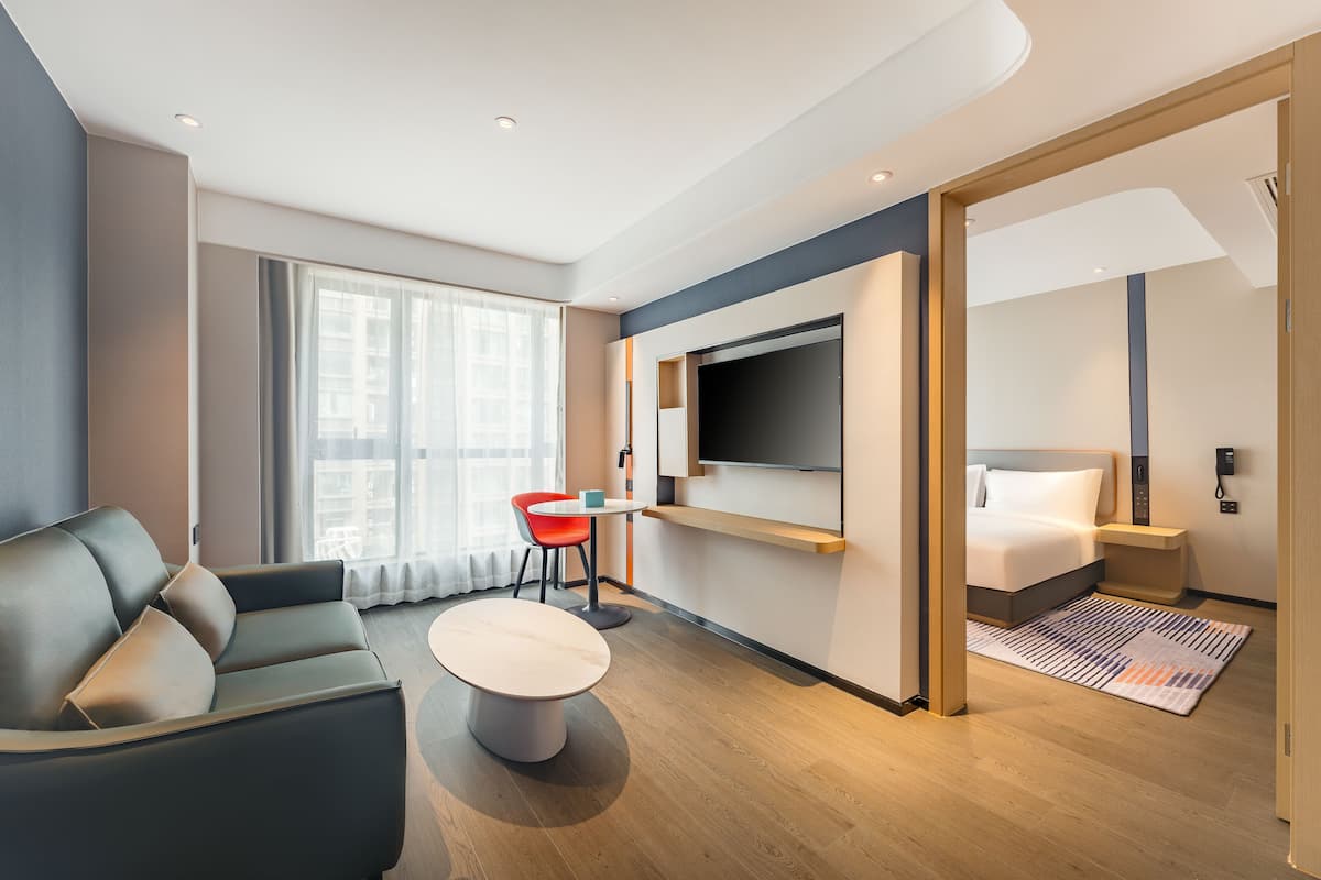 Una habitación de hotel moderna con sofá, una pequeña mesa, un televisor montado en la pared y una cama con mesita de noche.