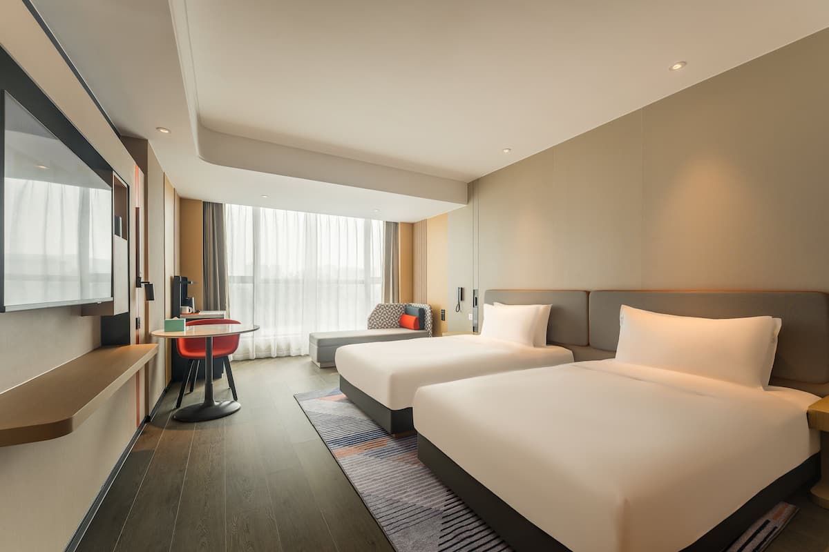 Habitación de hotel con dos camas, un escritorio, una silla y un ventanal grande.