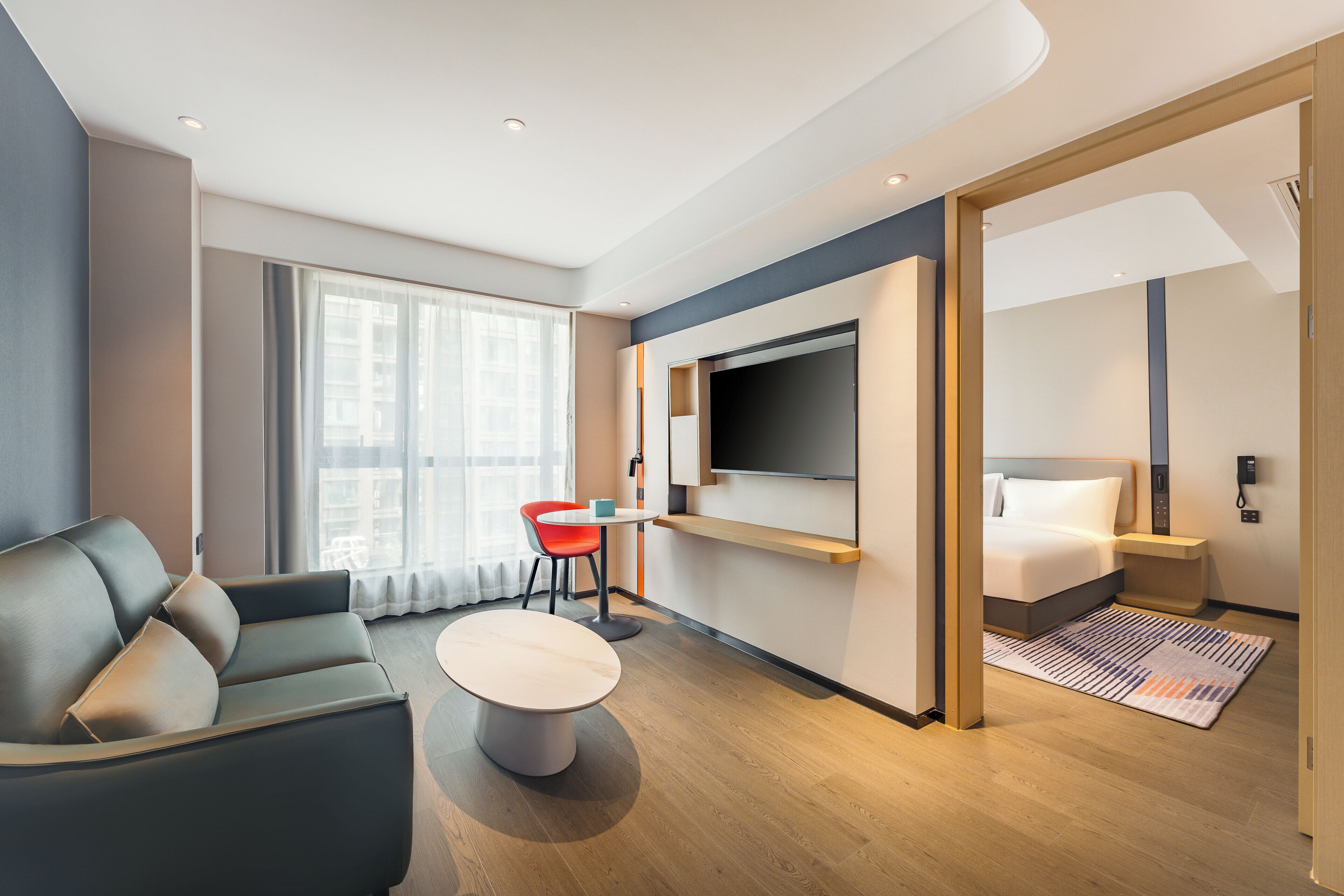 Une chambre d’hôtel moderne, équipée d’un canapé, d’une petite table, d’un téléviseur fixé au mur et d’un lit avec une tête de lit.