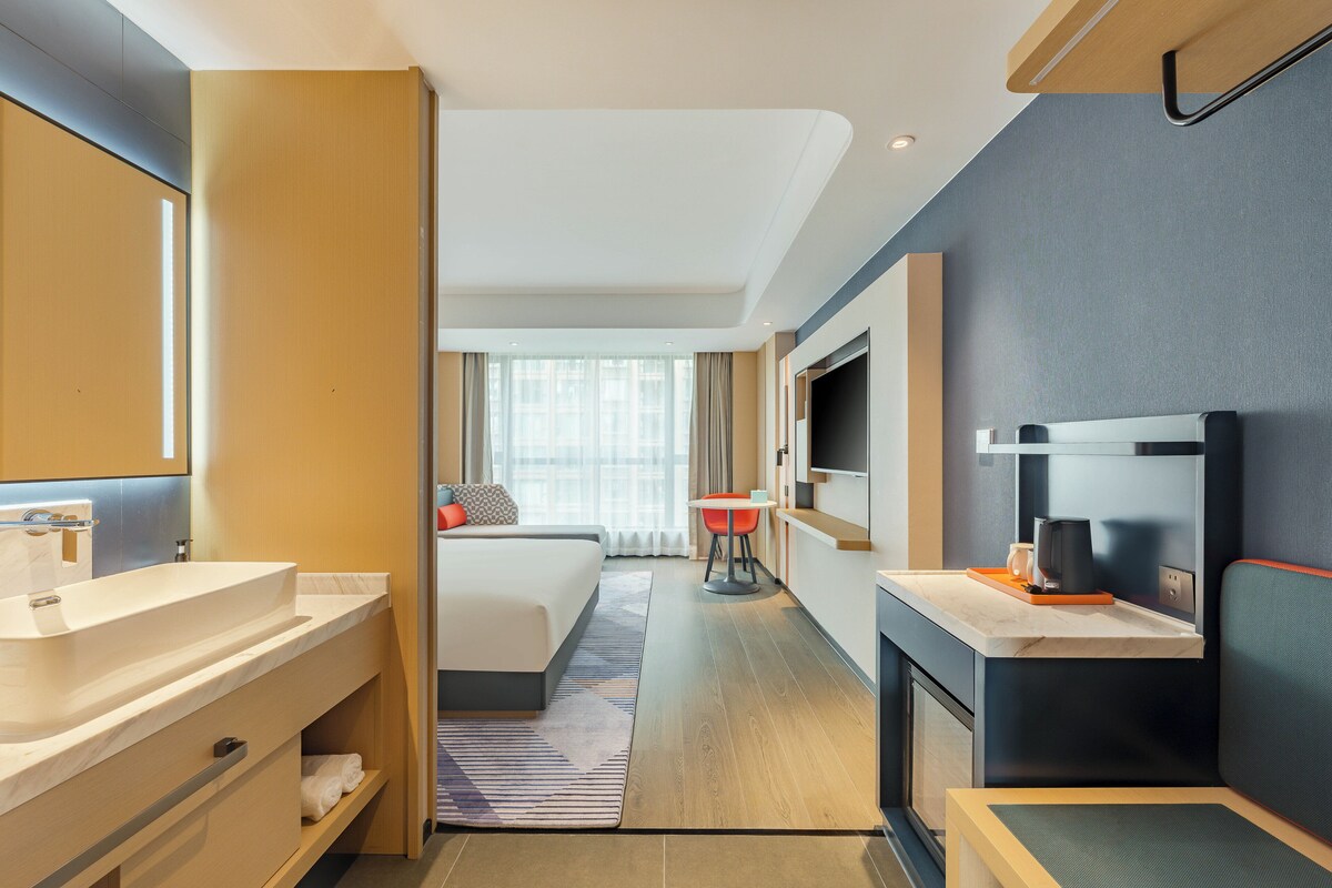 Een moderne hotelkamer met een groot bed, een badkamer met een wastafel en spiegel, een eettafel en een televisie.