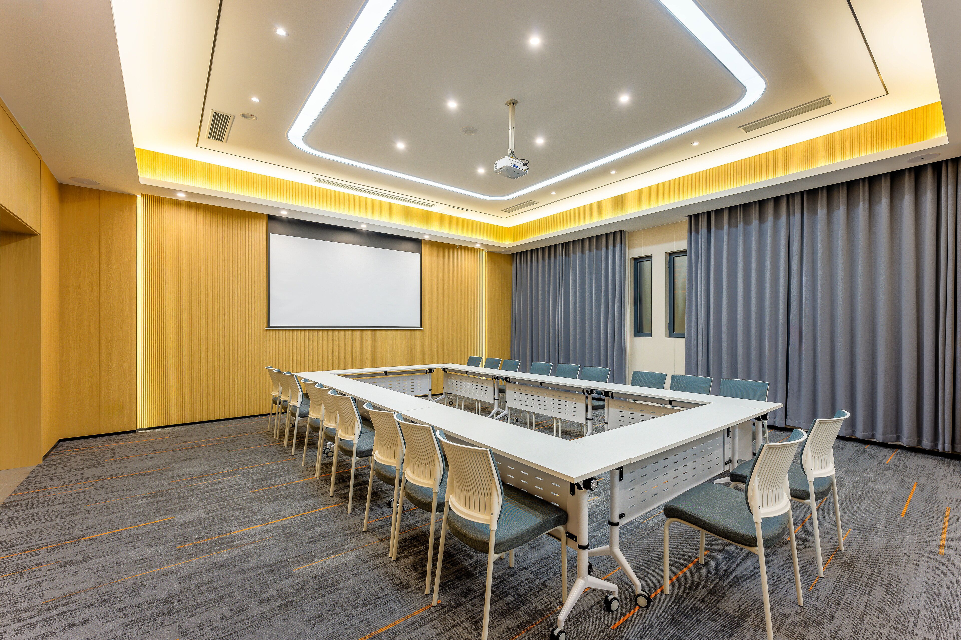 A conference room with a long table, chairs, a projector, and a screen.