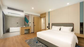 Una habitación de hotel moderna con una cama grande, un baño con bañera, tocador y escritorio.