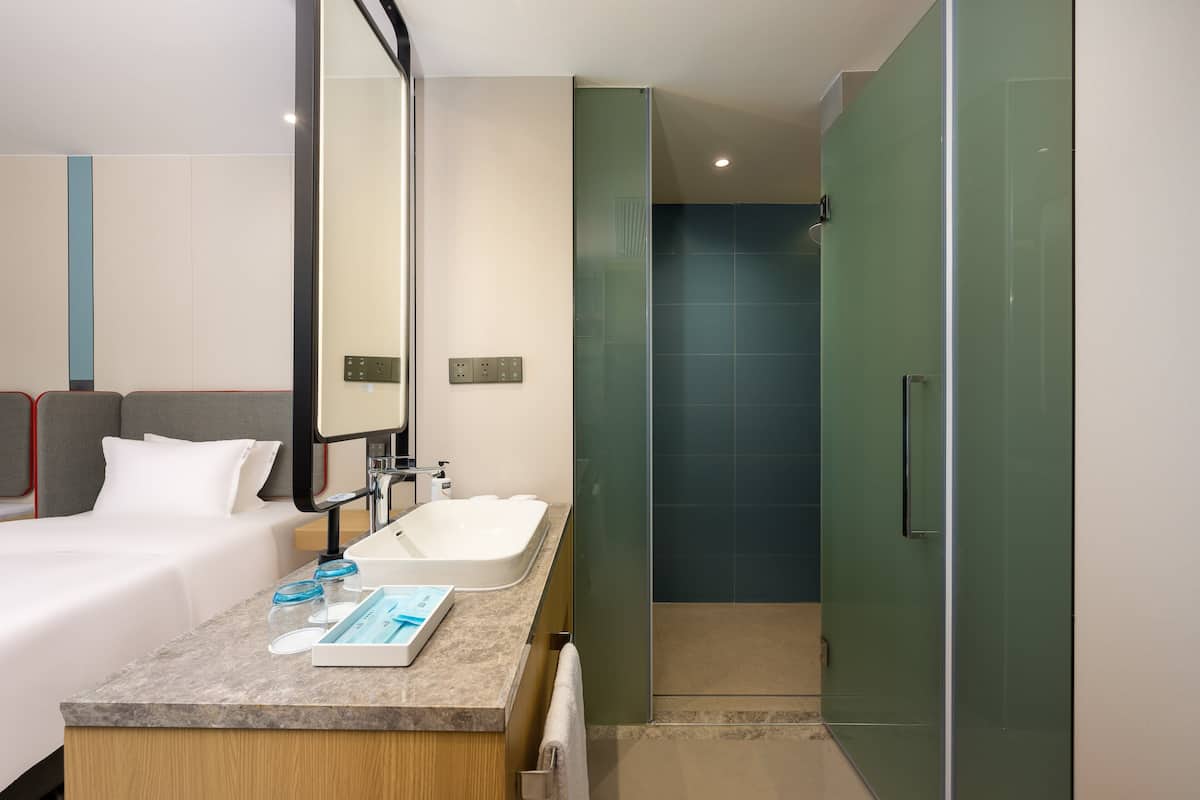 A modern hotel room with a bed, a bathroom with a sink, and a shower.
