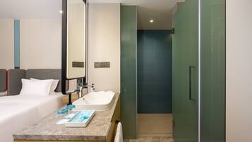 Una habitación de hotel moderna con cama, baño con lavamanos y ducha.