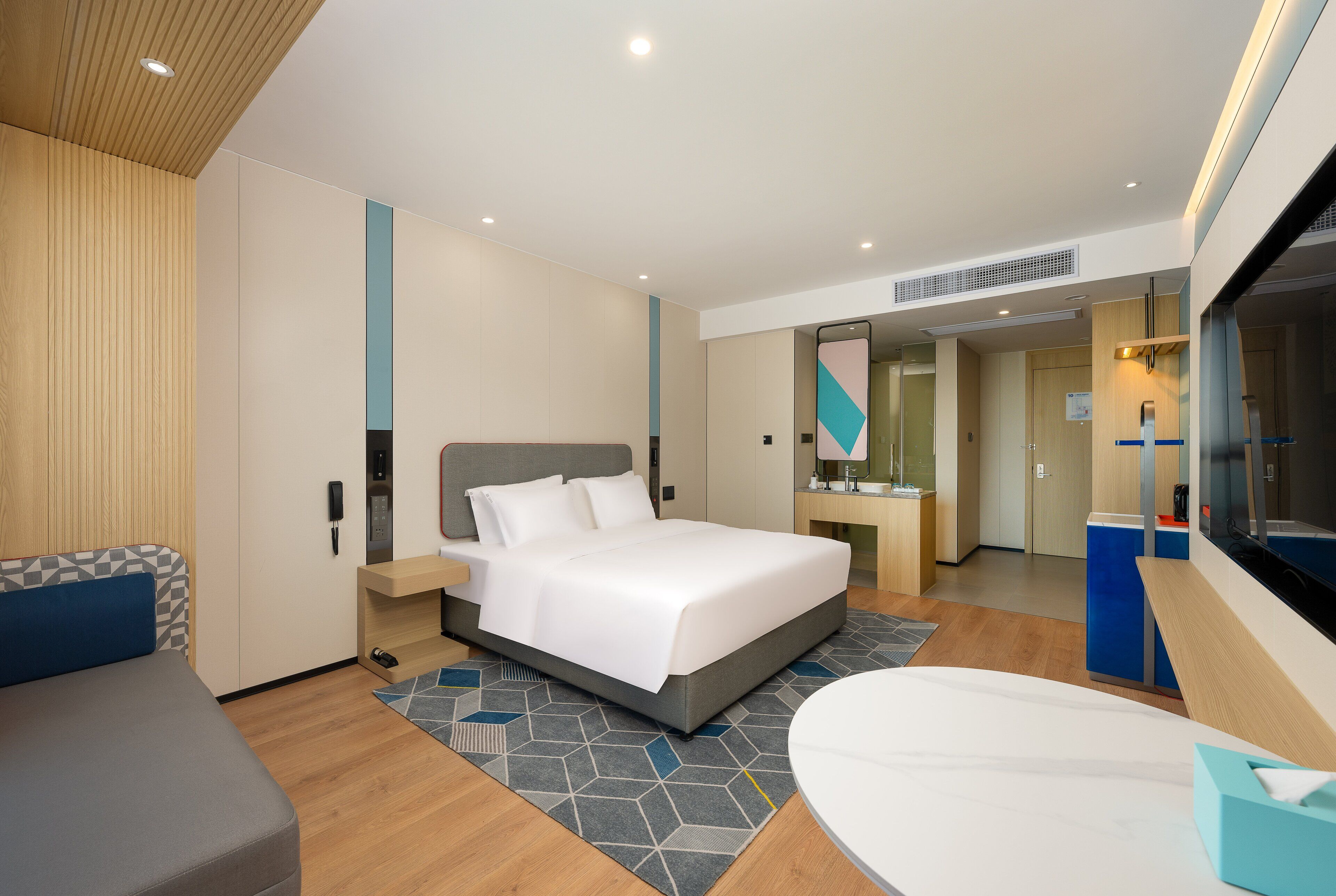 Ein modernes Hotelzimmer mit einem großen Bett, einem Schreibtisch, einem Sessel und einem kleinen Tisch.