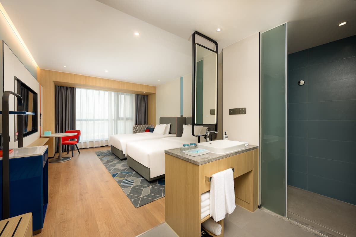 A hotel room with a bed, a desk, a chair, a bathroom with a sink and mirror, and a shower area.
