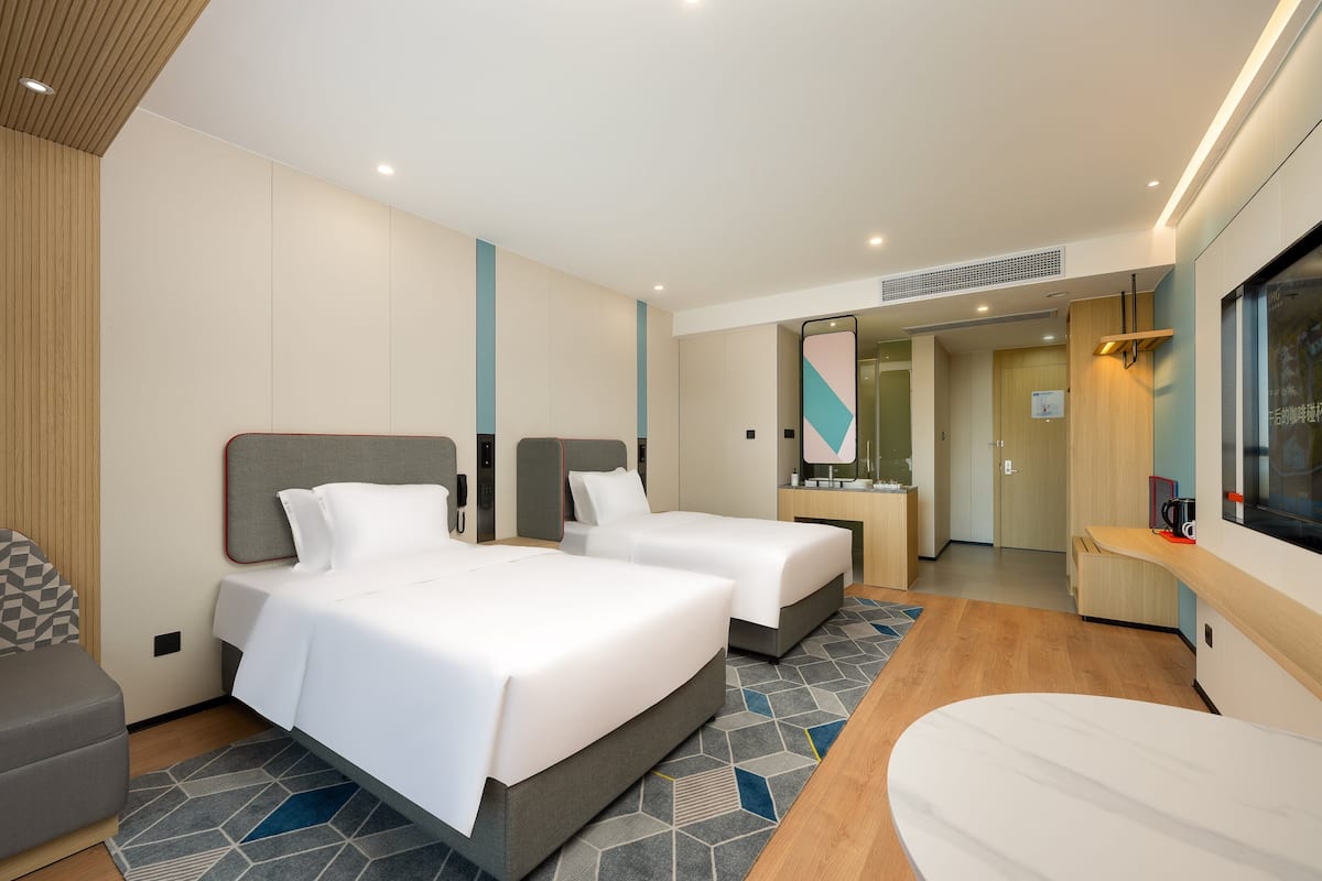 A modern hotel room with two beds, a sofa, a desk, and a large mirror.