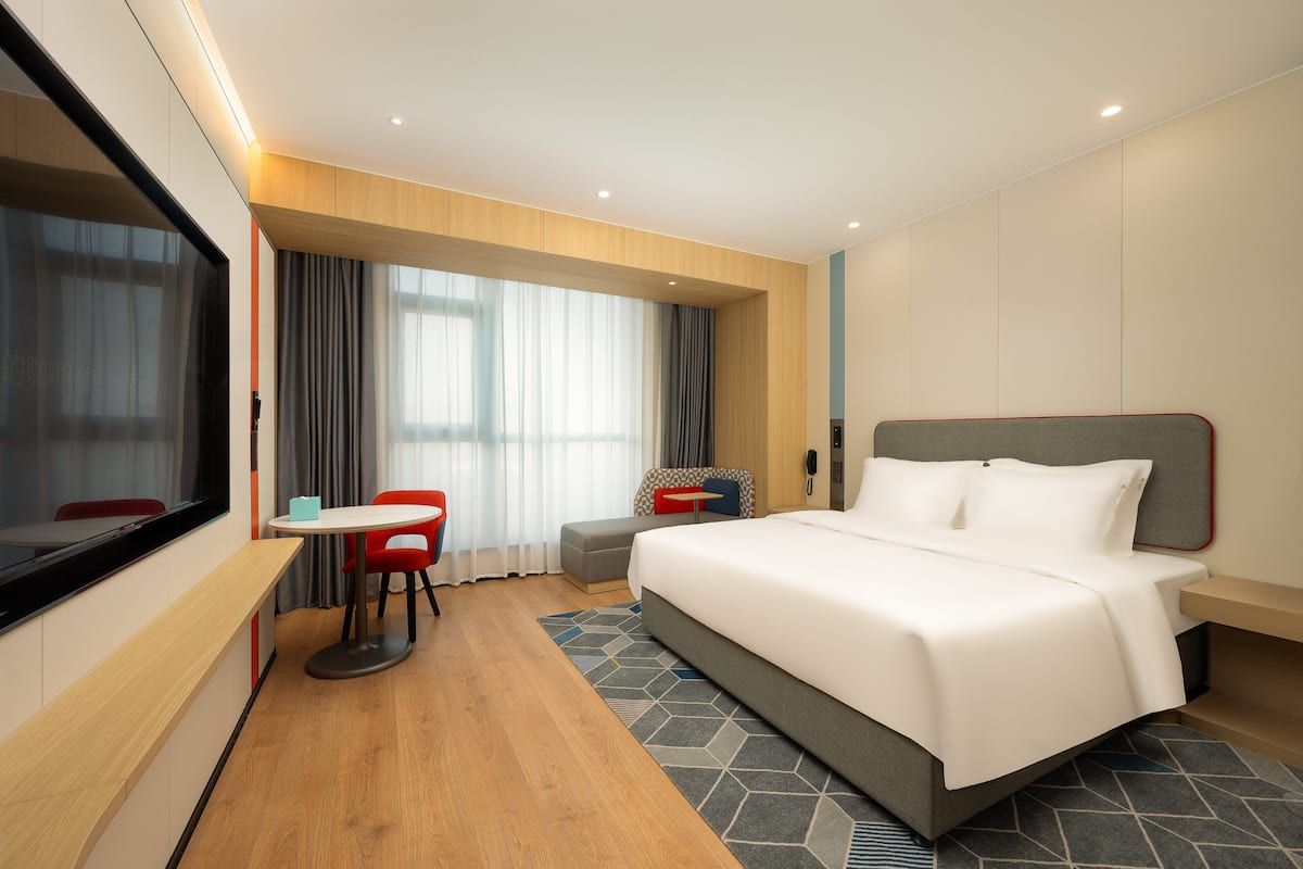 A modern hotel room with a large bed, a desk, and a chair.