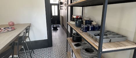 A kitchen with patterned floor tiles, a dining table with chairs, and shelves with kitchenware.