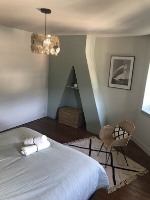 Une chambre à coucher comprenant un lit, une chaise, un luminaire suspendu, un tableau encadré et une petite étagère.