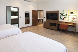 A hotel room with two beds, a TV, a desk with a chair, and artwork on the wall.