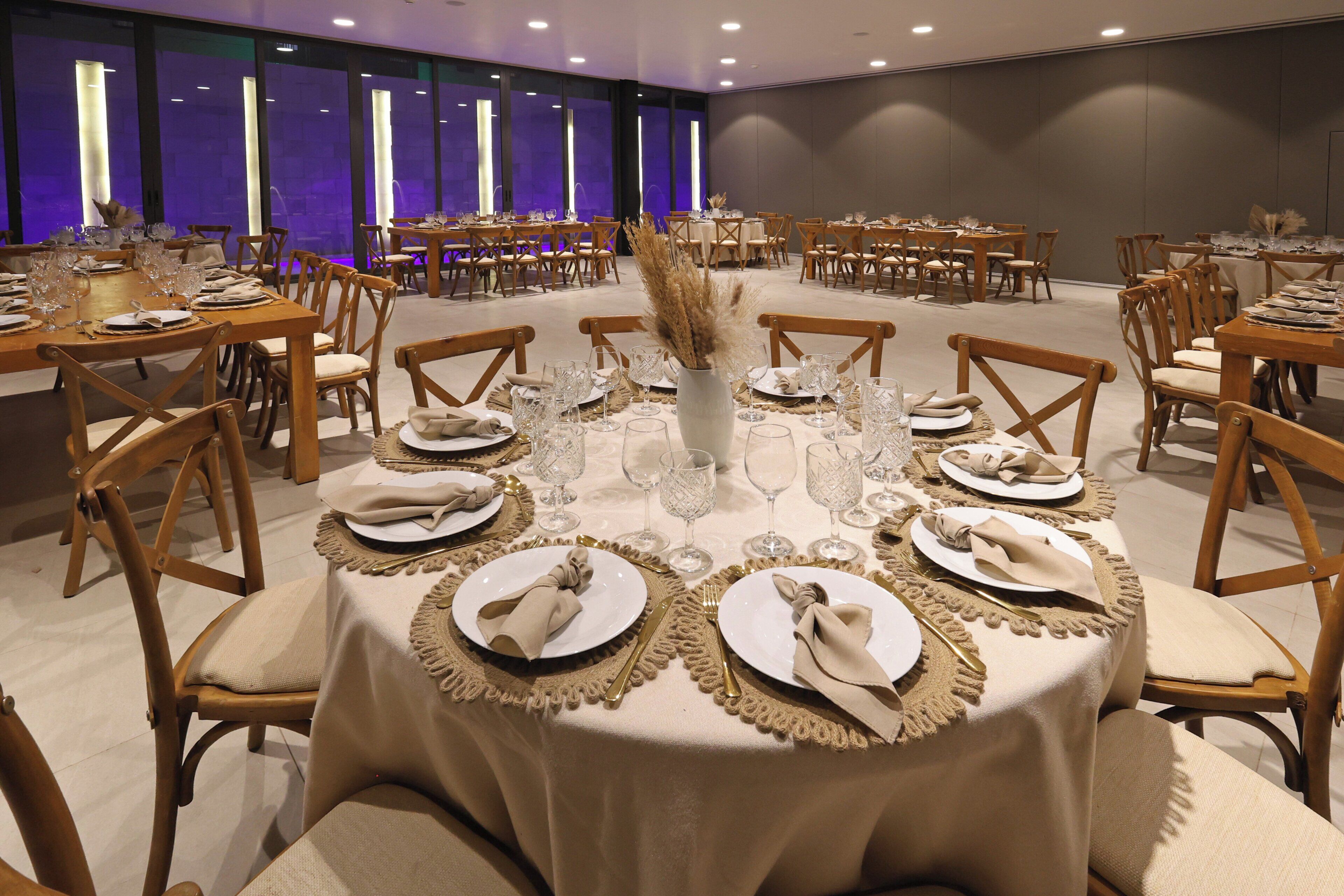 Una sala de banquets amb taules rodones preparades per sopar, amb estovalls beix, subjectes daurats per als draps i un ram central de plantes seques.