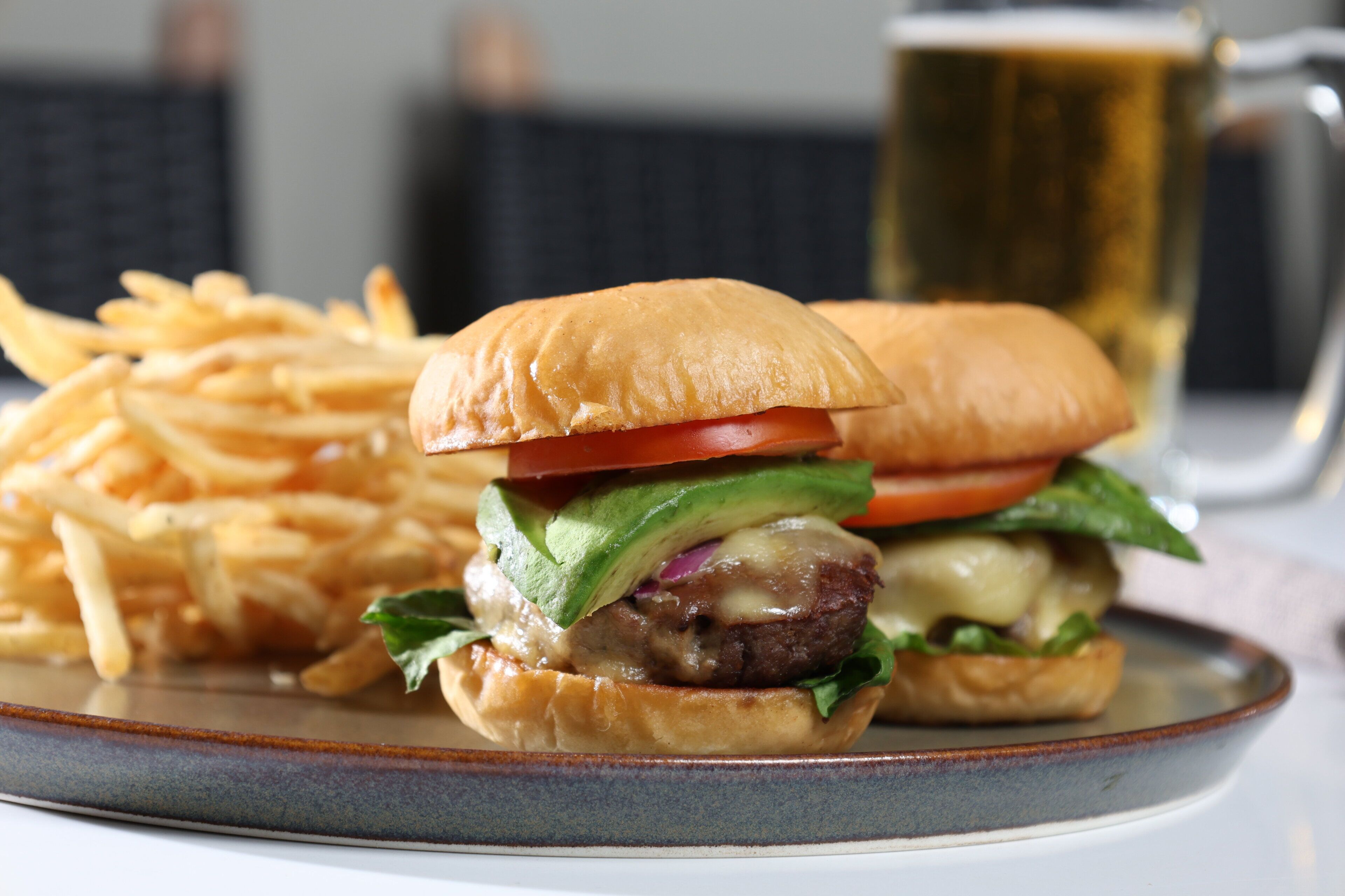 A plate with a burger and fries, and a beer mug in the background.
