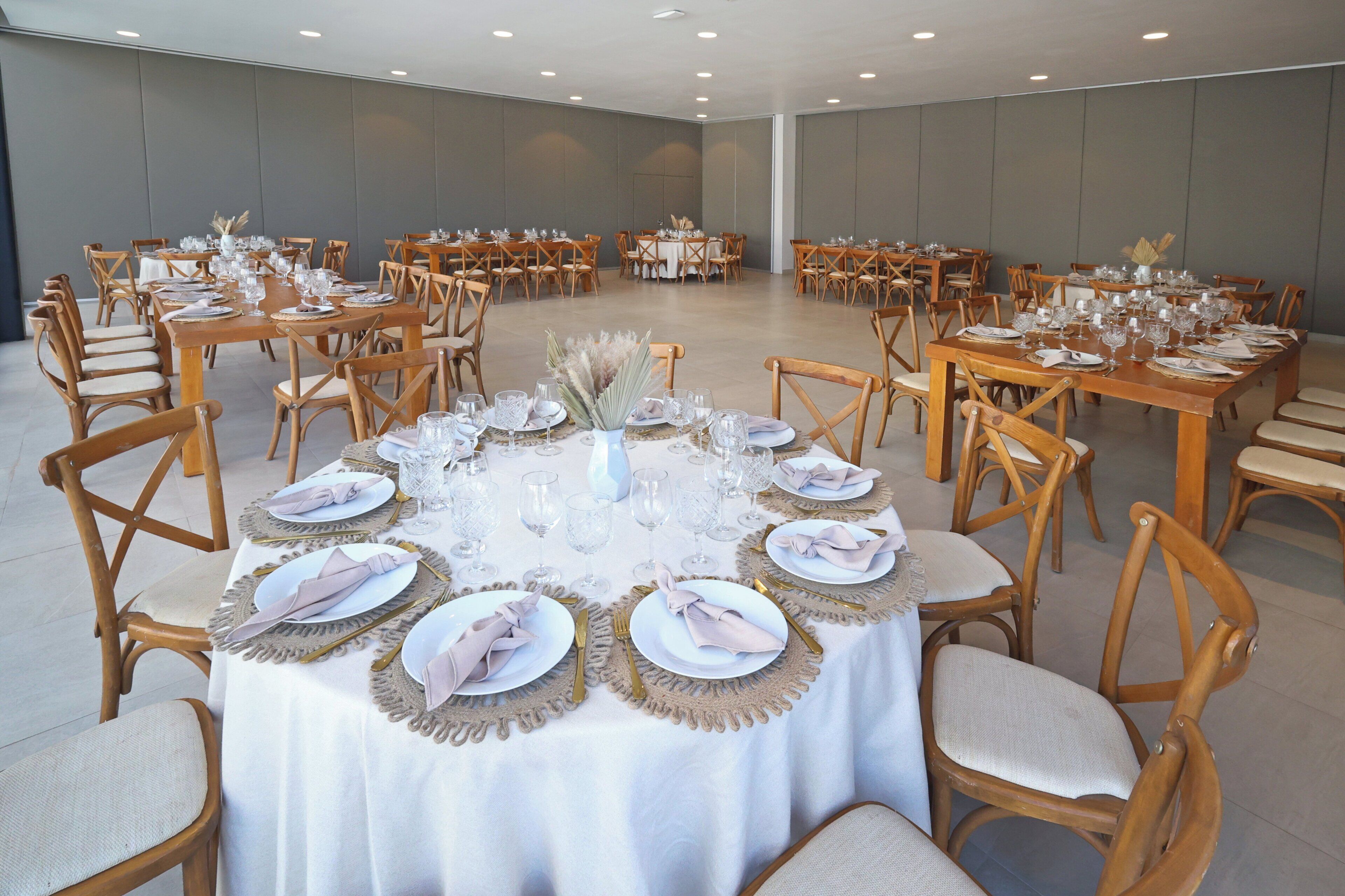 A large banquet hall with multiple round tables set for dining, each with white tablecloths, wooden chairs, and neatly arranged table settings.